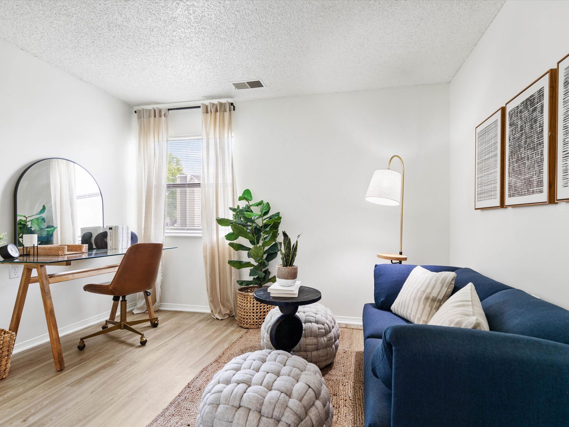 Living room with desk, blue sofa, and decorative items; neutral tones and natural light.