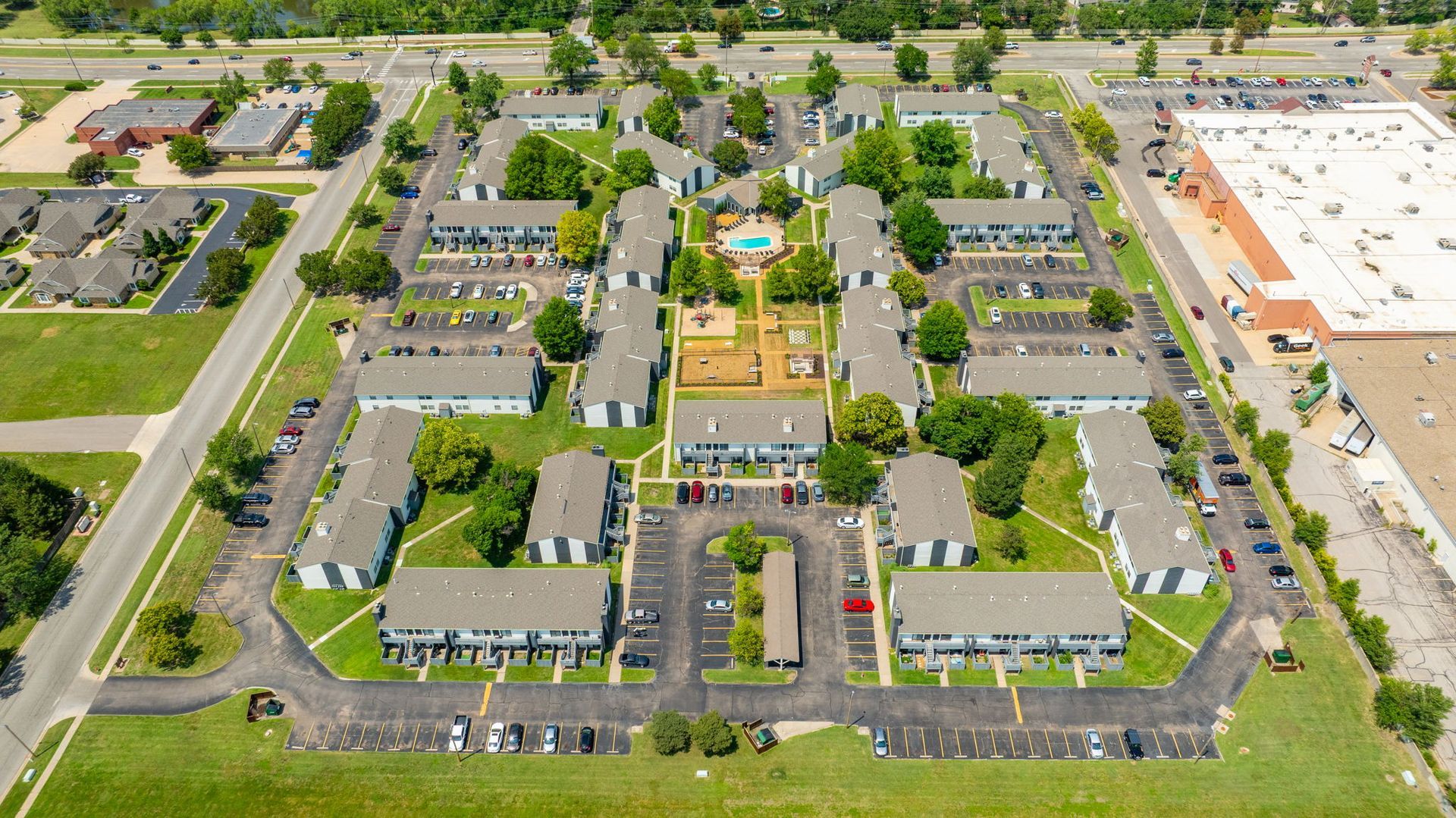 Aerial view of an apartment complex with multiple buildings, a central courtyard, and parking areas.