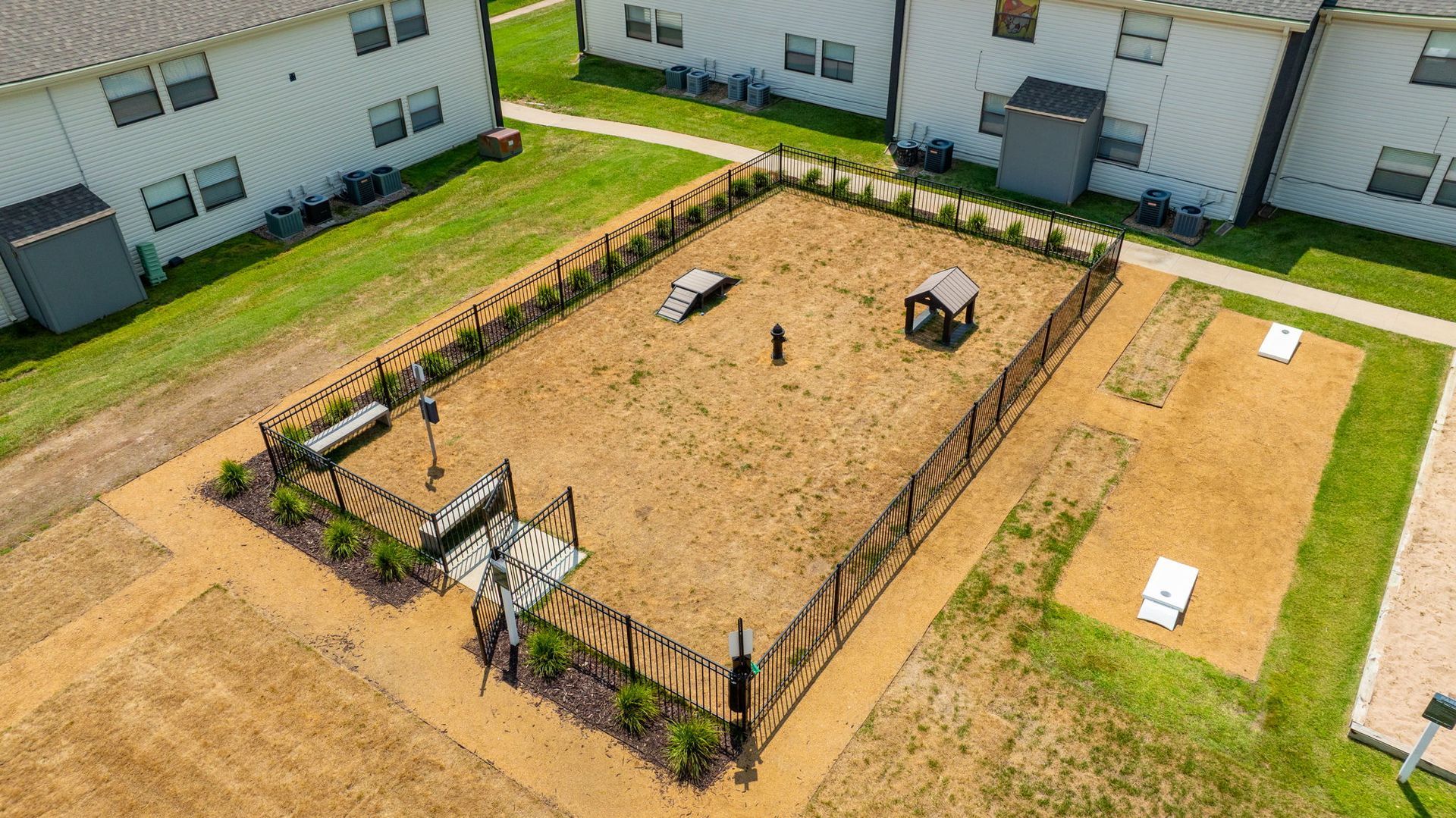 Aerial view of a dog park with fenced-in play area, agility equipment, and a small dog house.