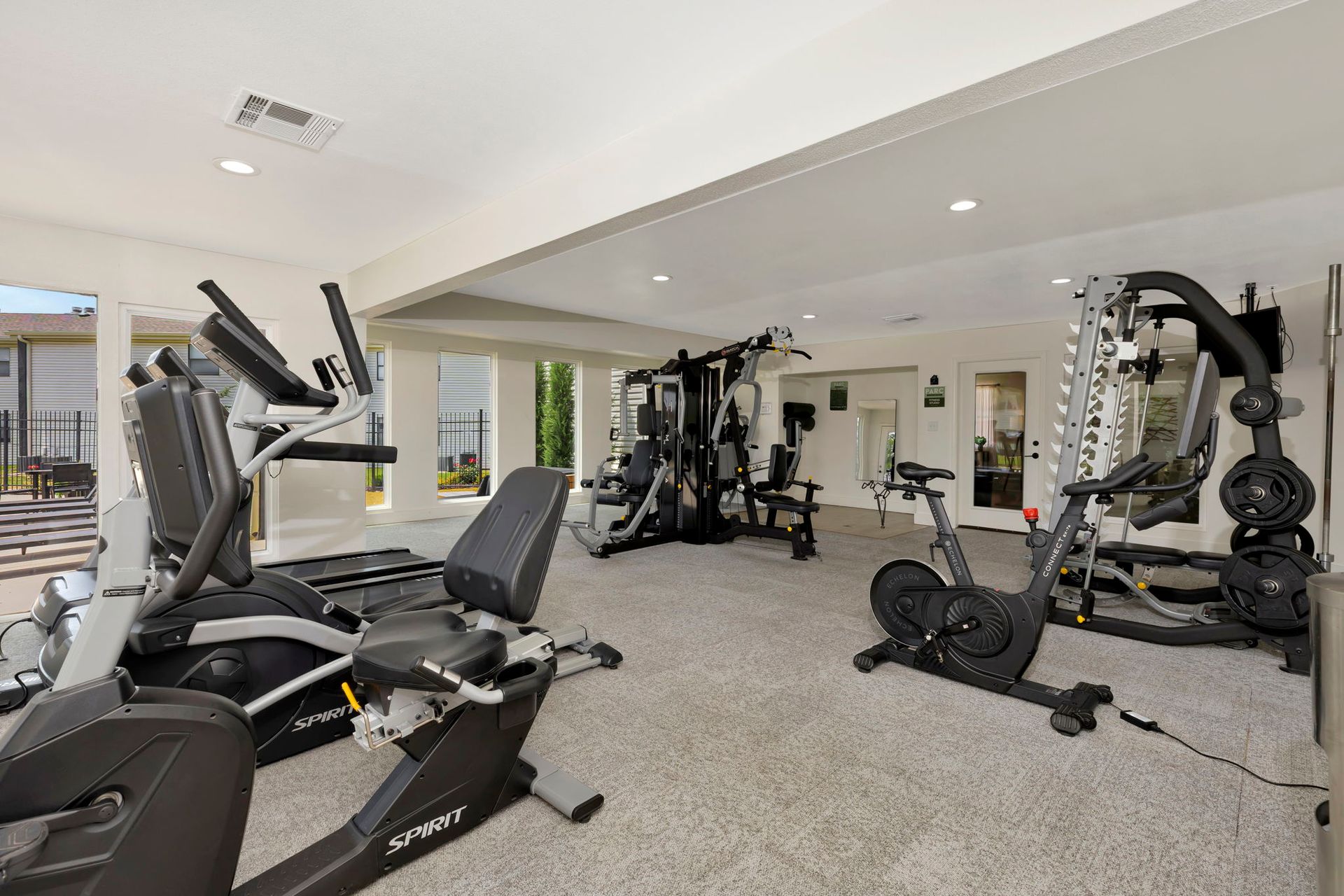 Gym with exercise equipment on gray carpet. Cardio machines and weight stations are visible.
