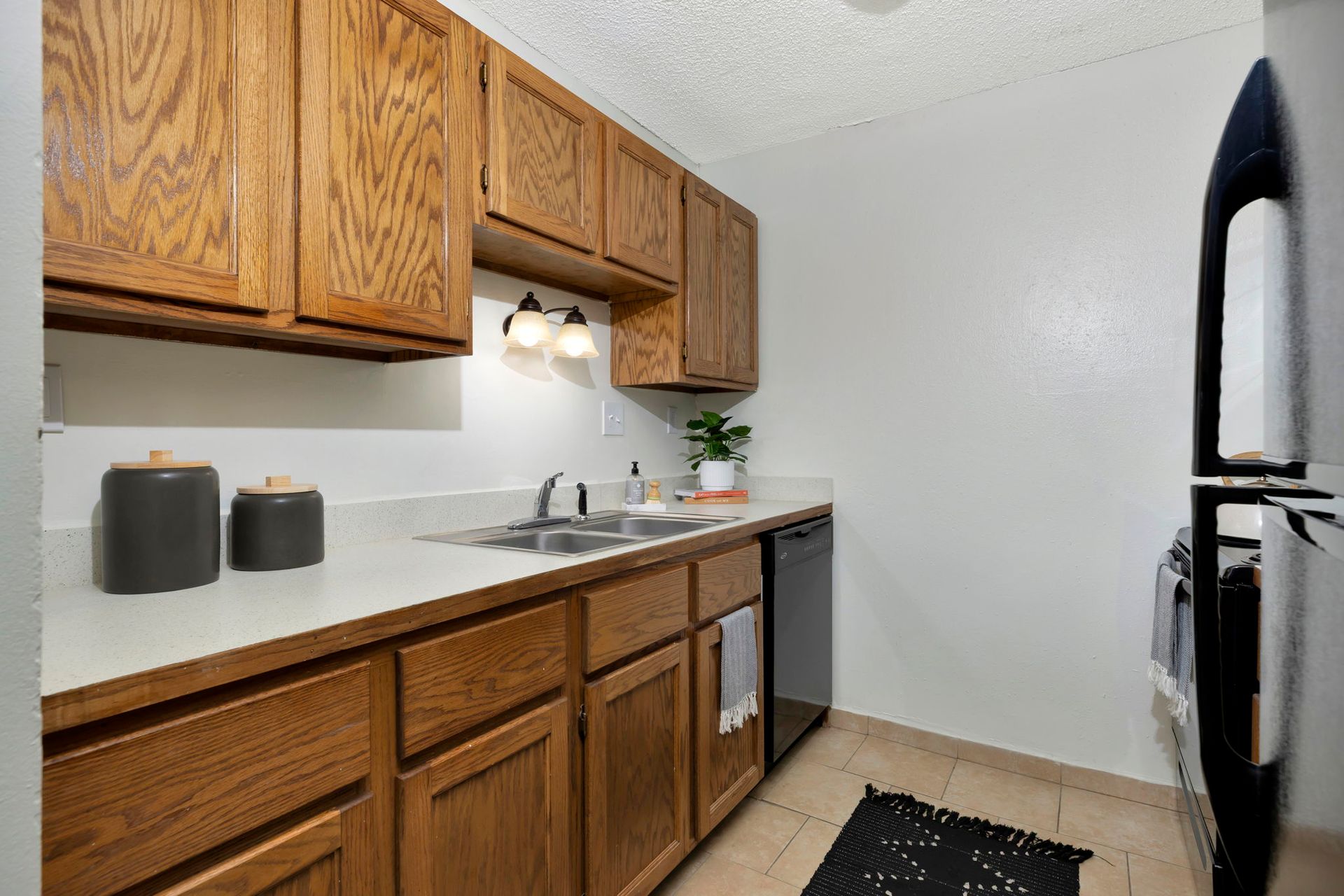 Kitchen with wooden cabinets, white countertop, stainless steel sink, black appliances, and beige tile floor.