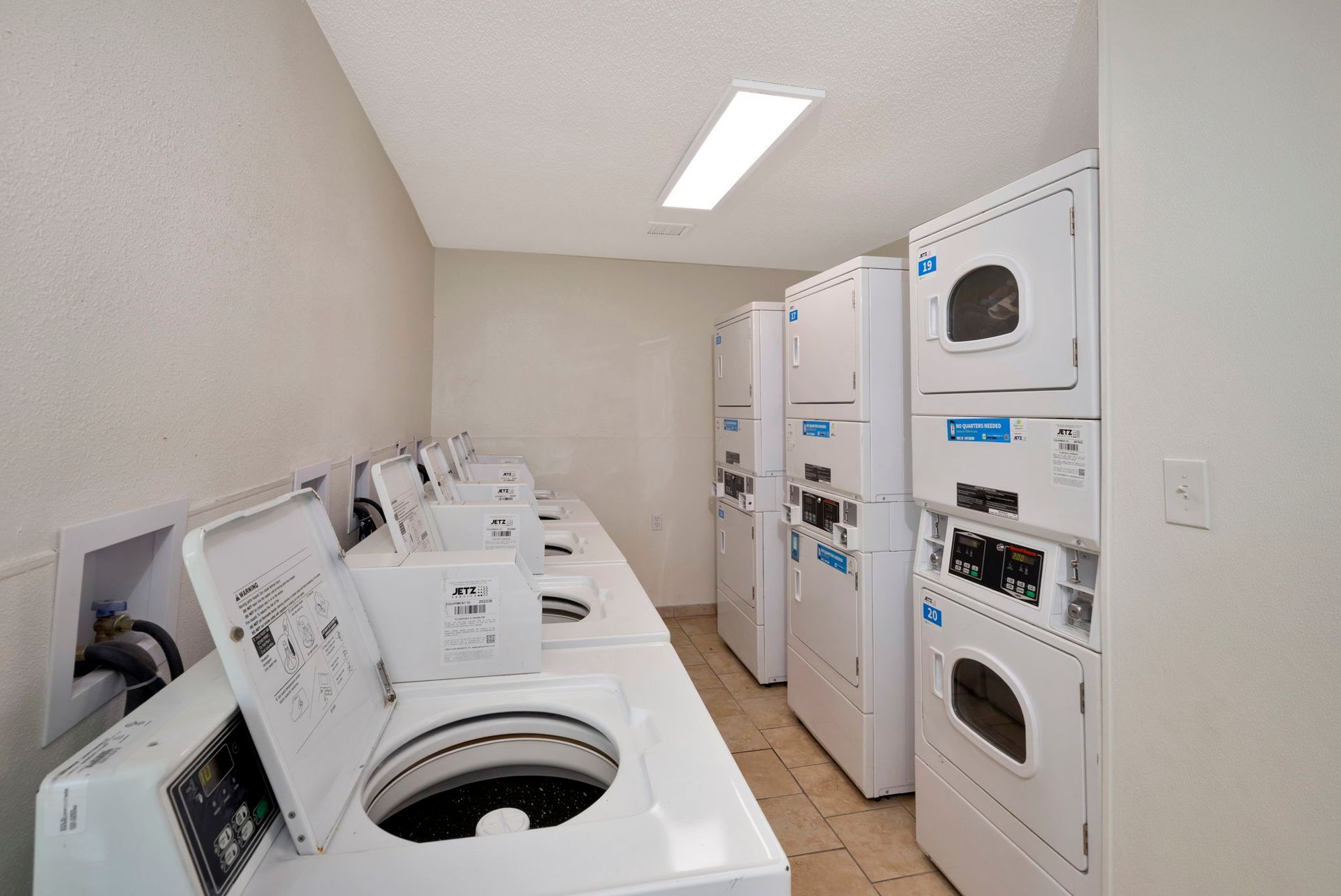 Laundry room with rows of washing machines and dryers. White appliances against white walls.