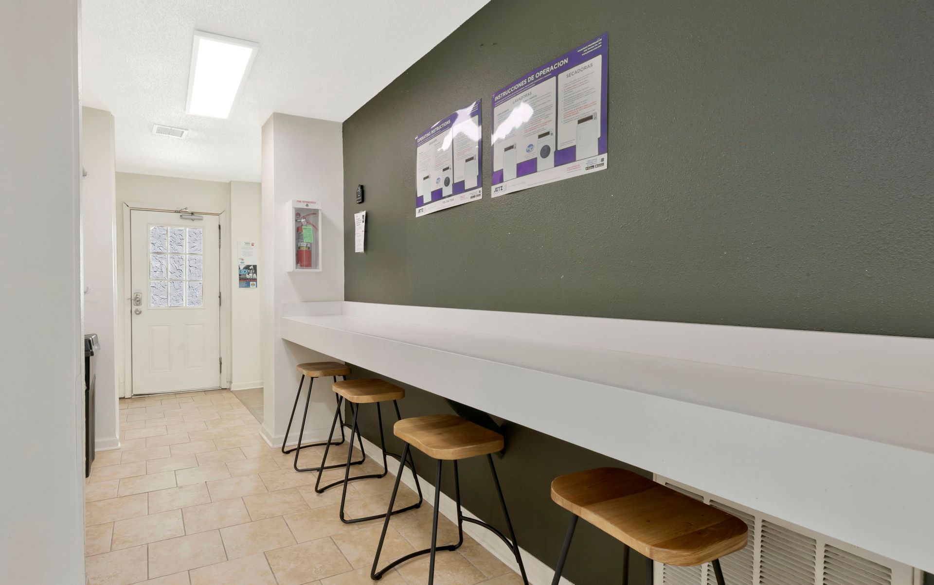 A hallway with a counter and stools, papers on the wall, and a door at the end.