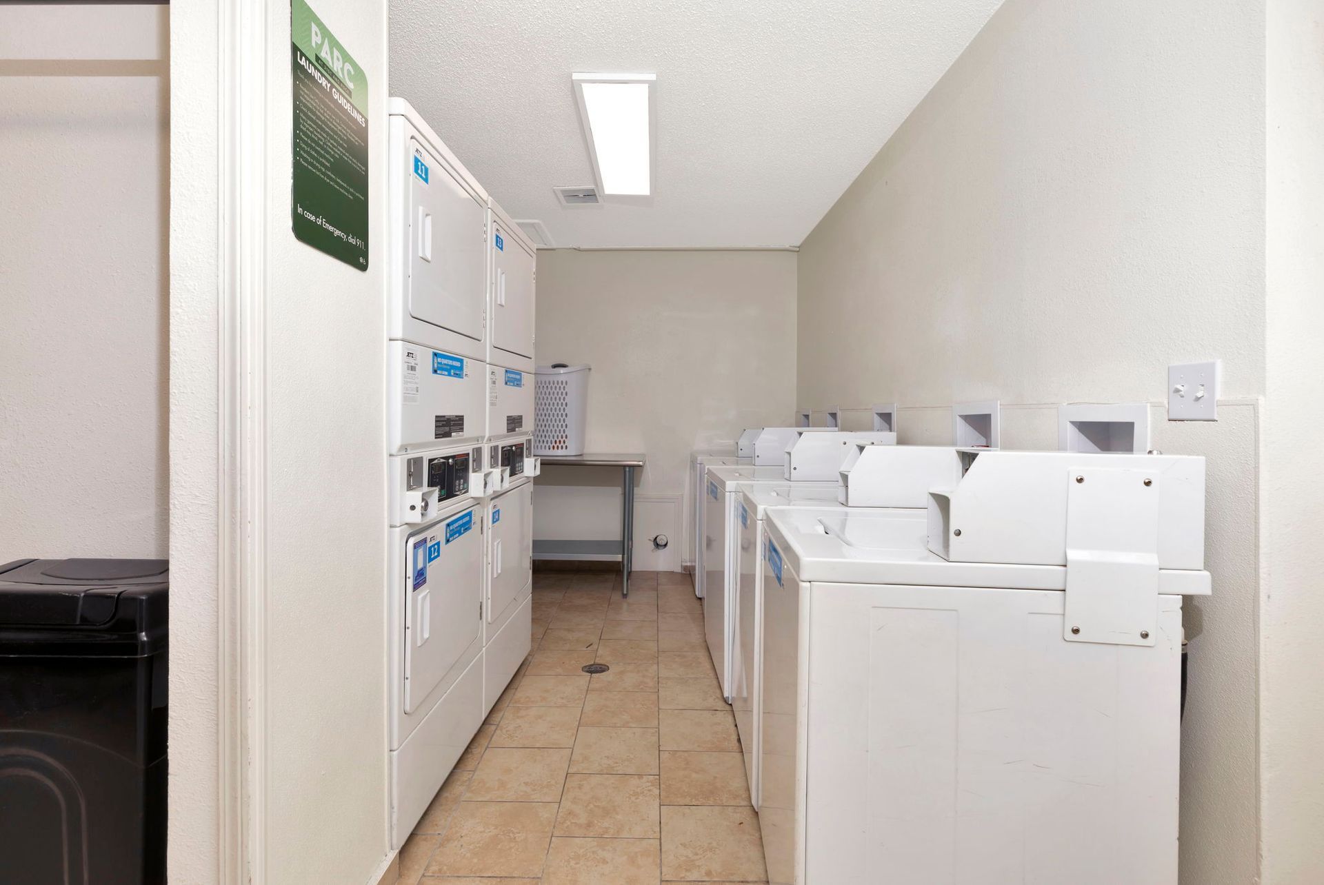 Laundry room with white washers and dryers, beige tile floor, and fluorescent lighting.