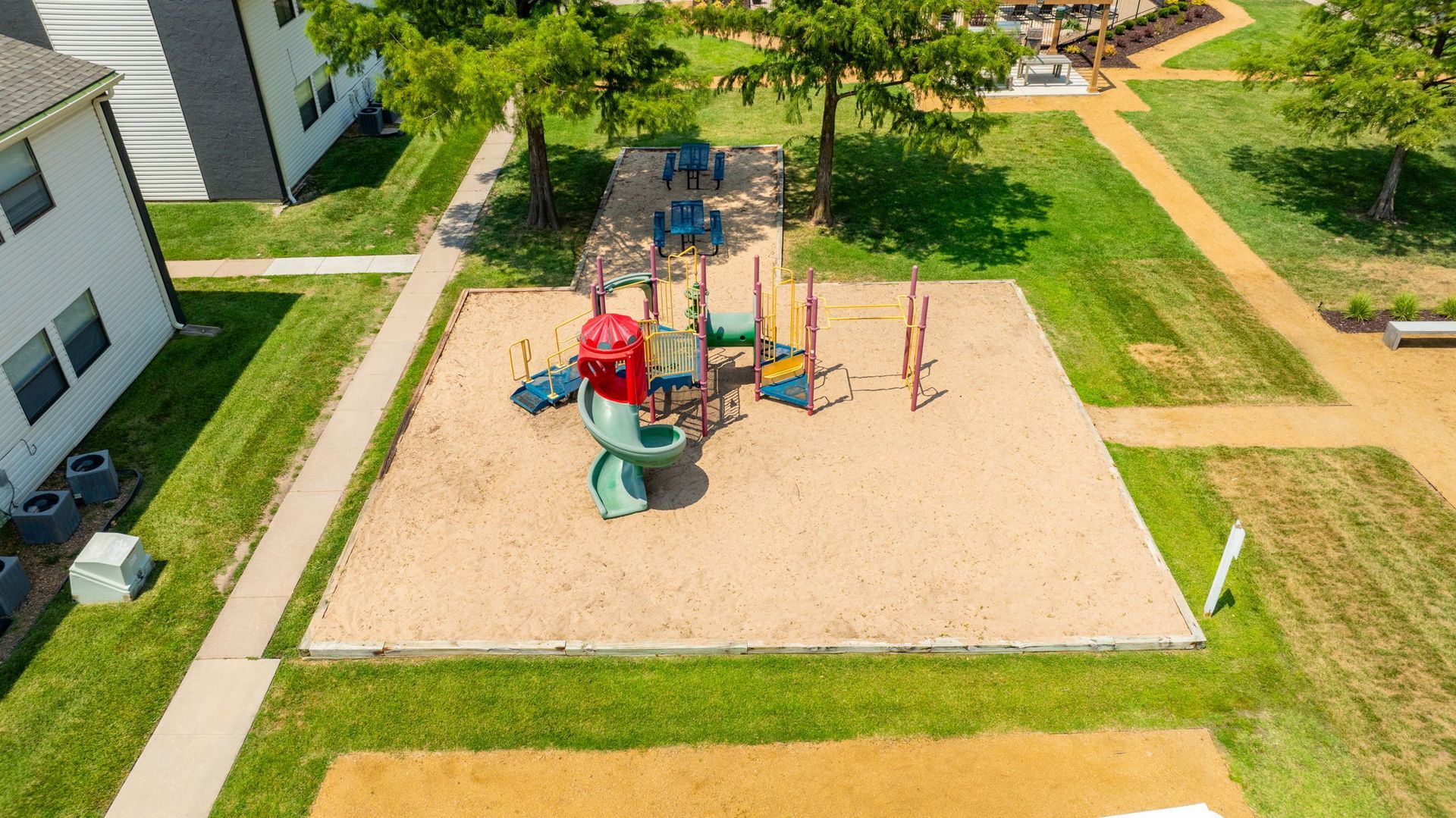 Playground in a grassy area, with slides, climbing structures, and surrounding walkways.