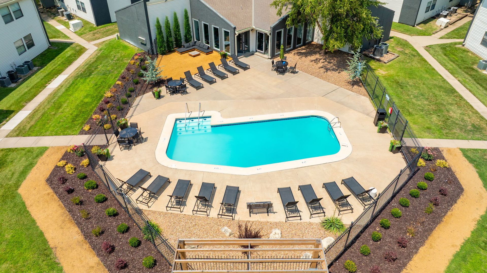 Aerial view of a pool surrounded by lounge chairs, landscaping, and a clubhouse.