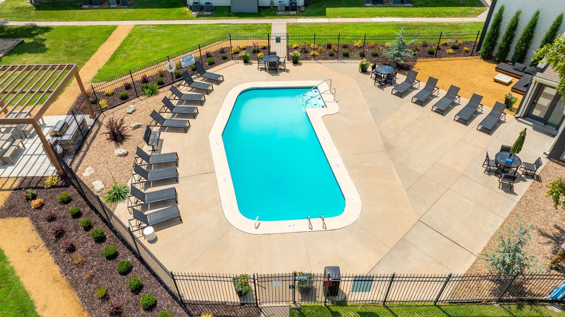 Swimming pool with lounge chairs, surrounded by landscaping and fence.