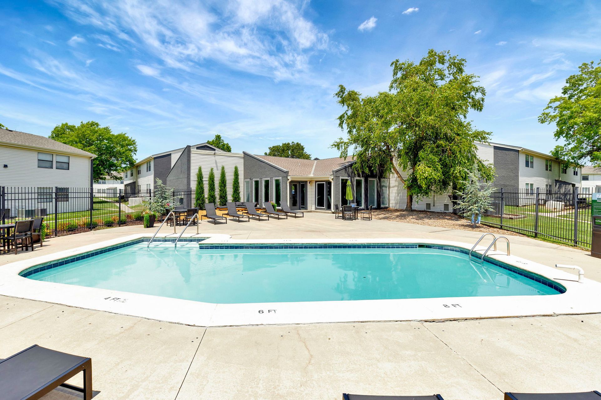 Pool surrounded by lounge chairs, building in background, blue sky.