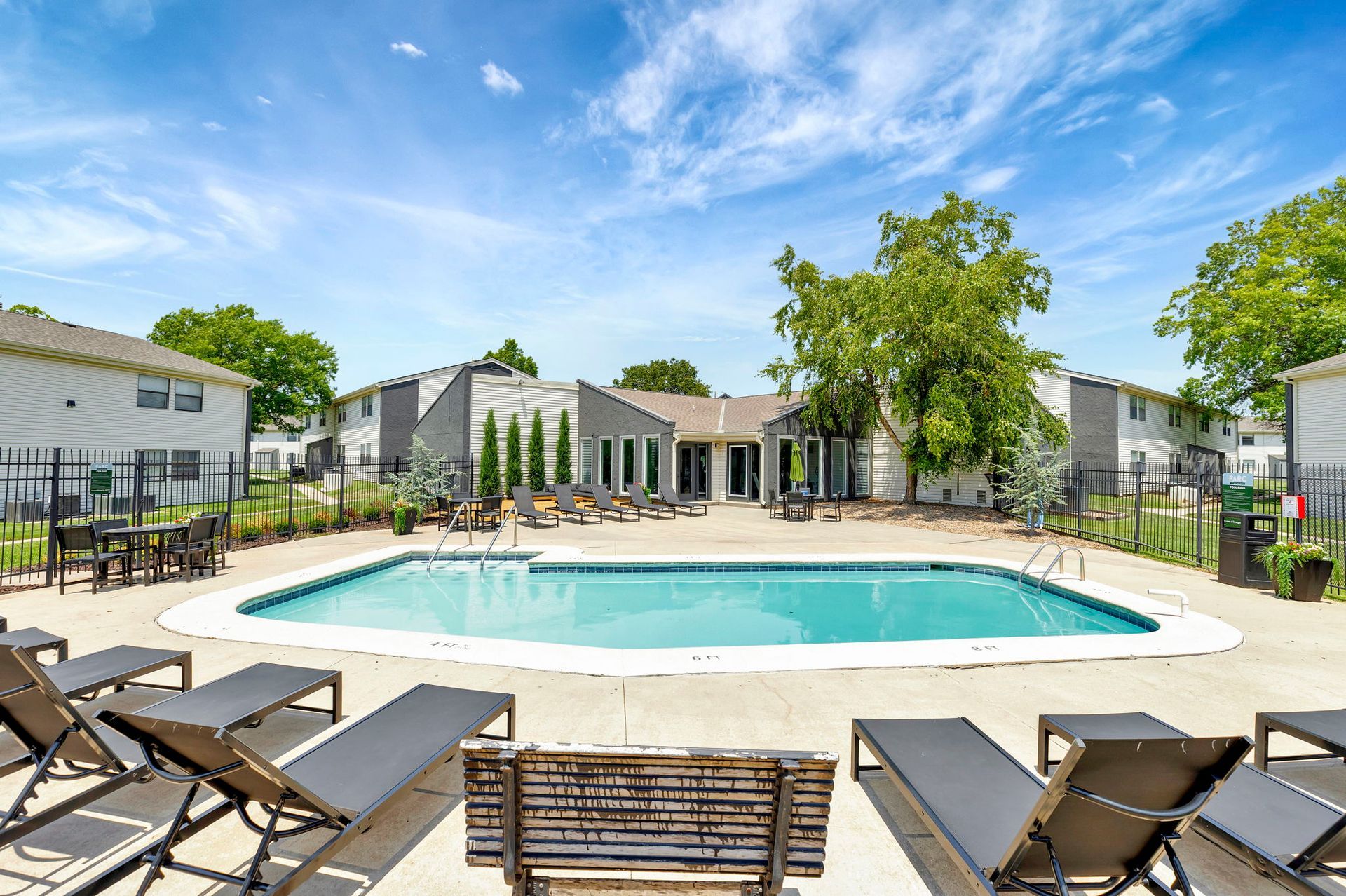 Swimming pool with lounge chairs, surrounded by apartments under a blue sky.