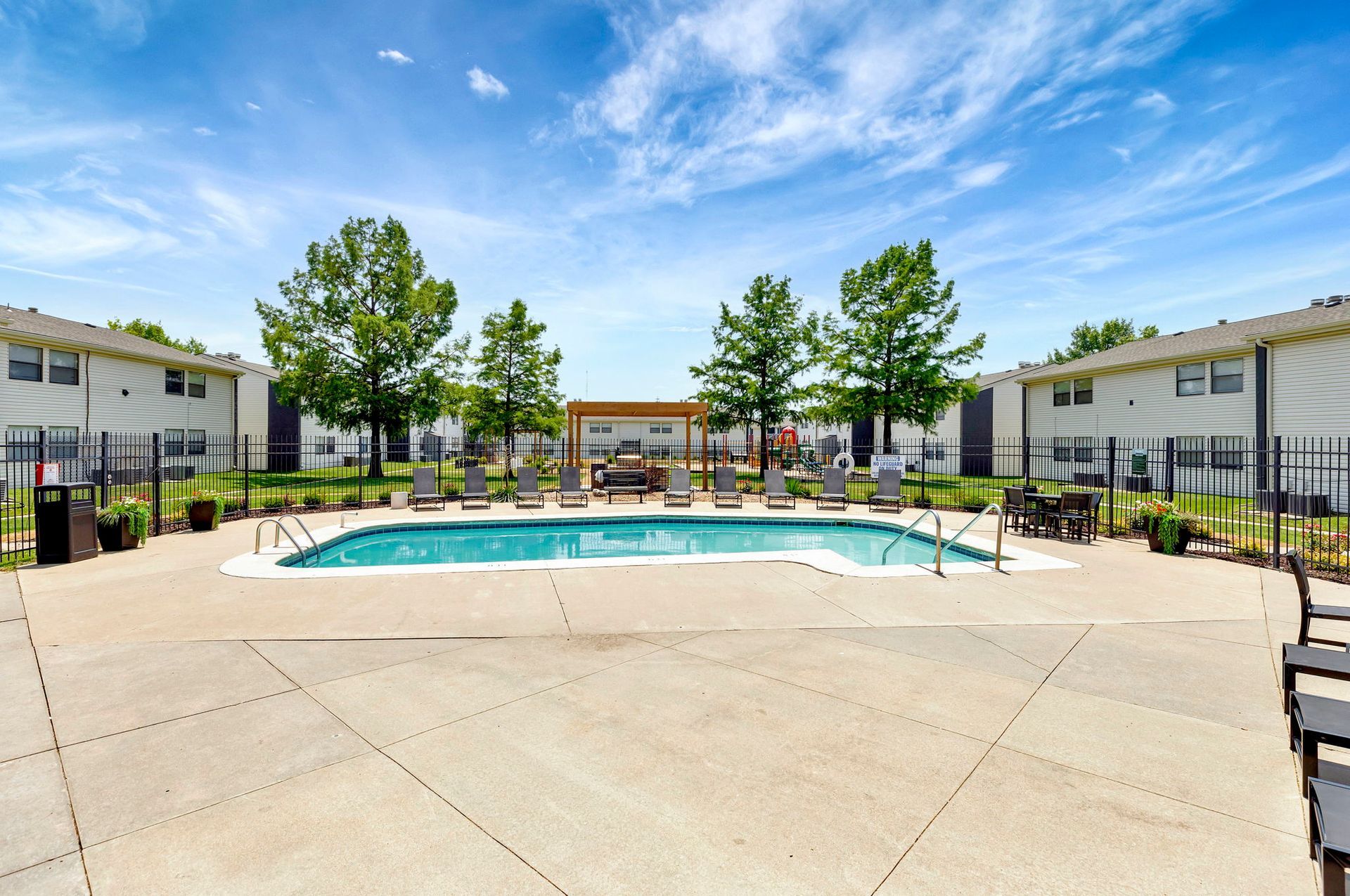 Swimming pool with lounge chairs, surrounded by apartments under a blue sky.
