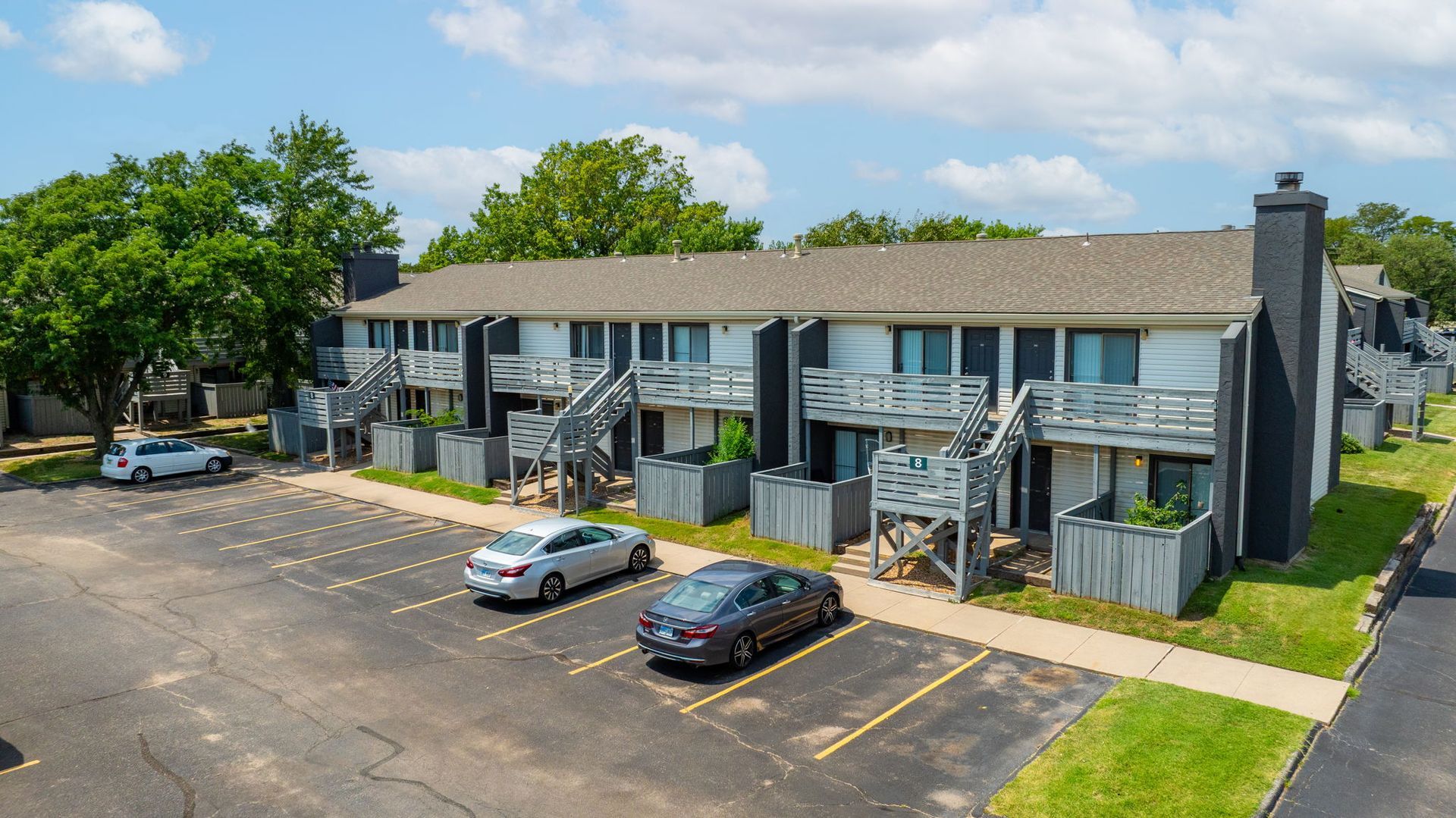 Apartment complex with cars parked in front. Gray and white buildings with wooden staircases.