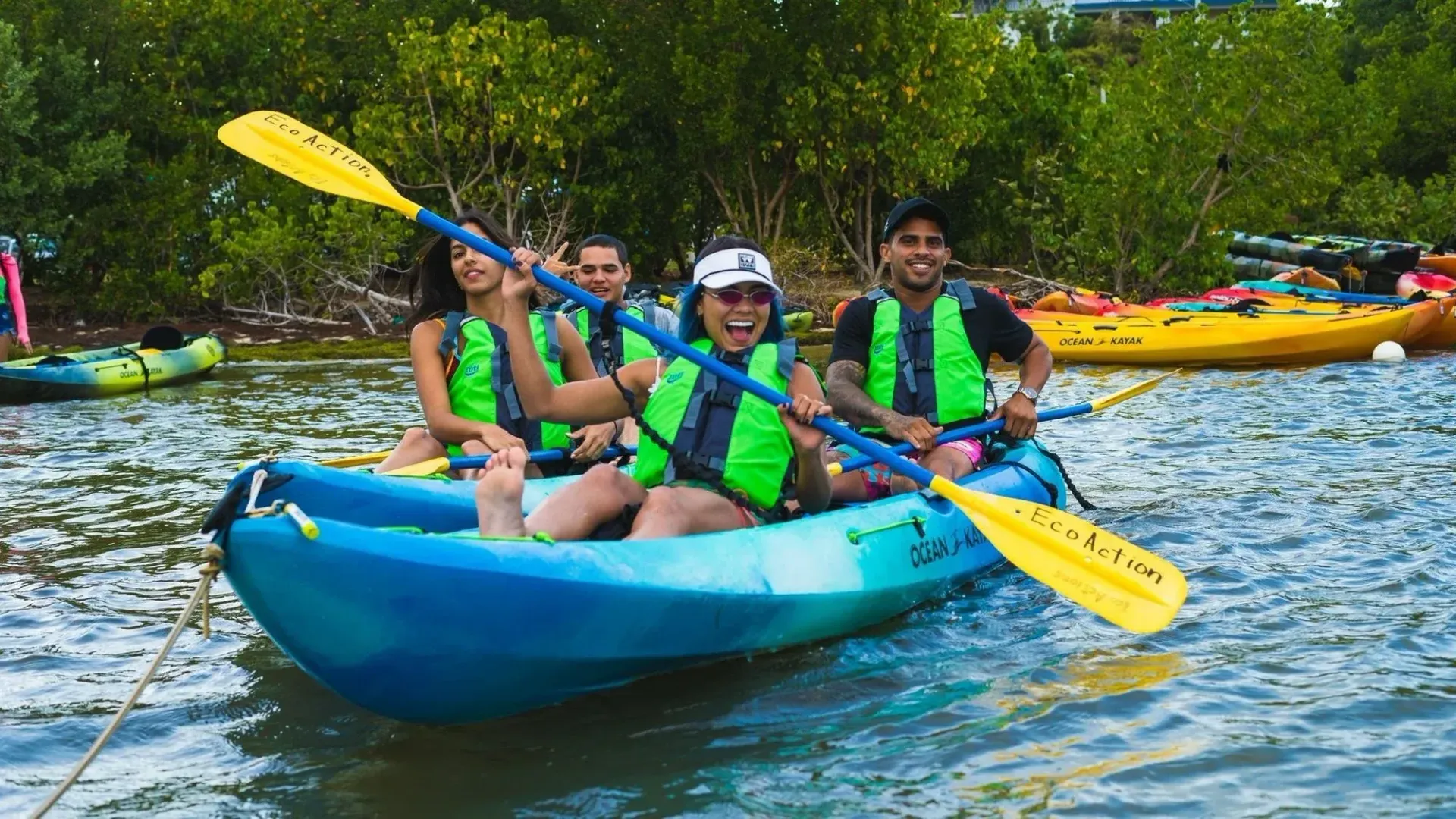 Three people paddling a blue kayak on choppy water with yellow oars