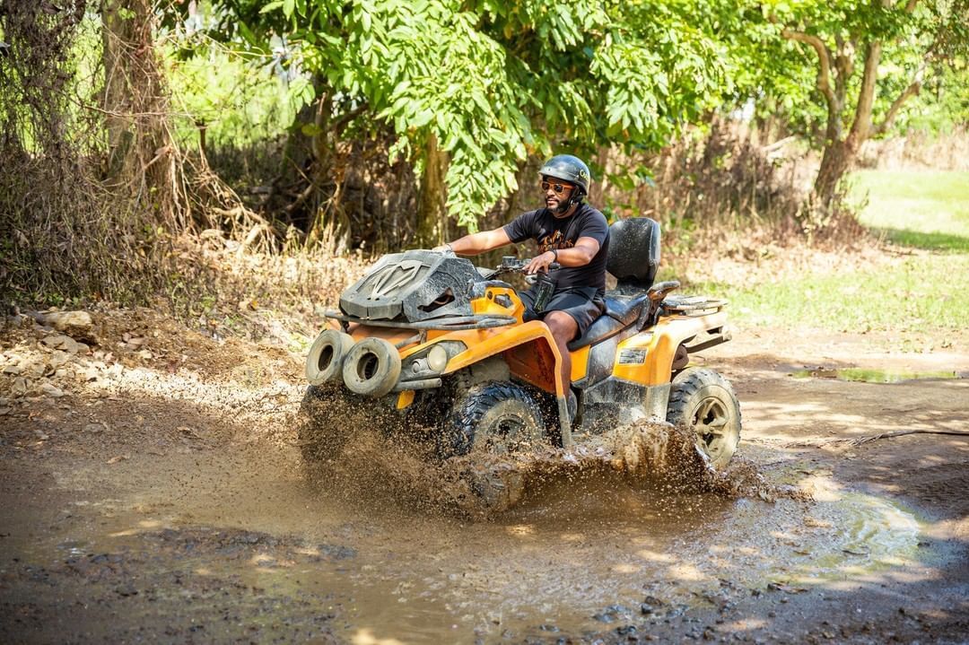 ATV rider splashes through a muddy forest trail in an orange off-road vehicle.