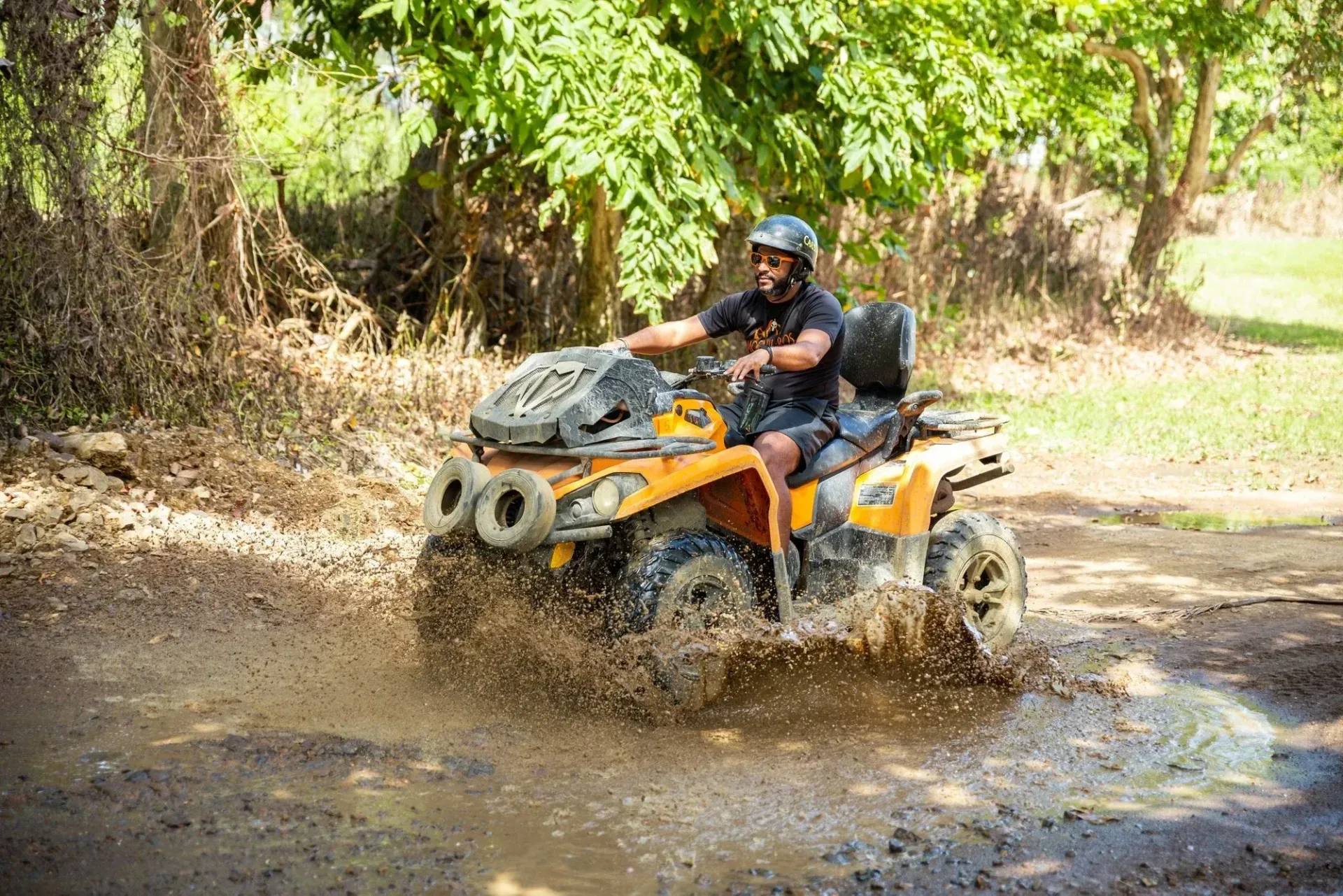 Person riding an orange ATV through muddy water on a forest trail