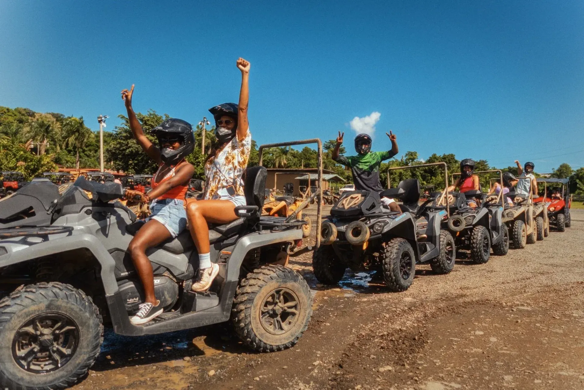 ATV convoy with riders raising hands on a dusty trail under a clear blue sky