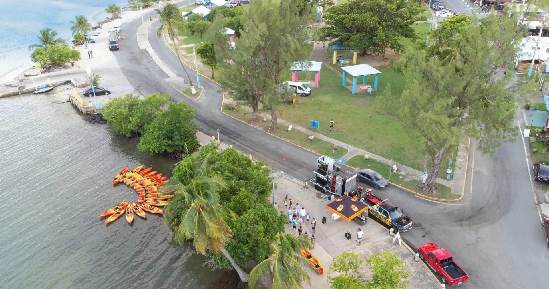 Aerial view of a lakeside road with a stranded car and emergency workers near orange rescue boats.