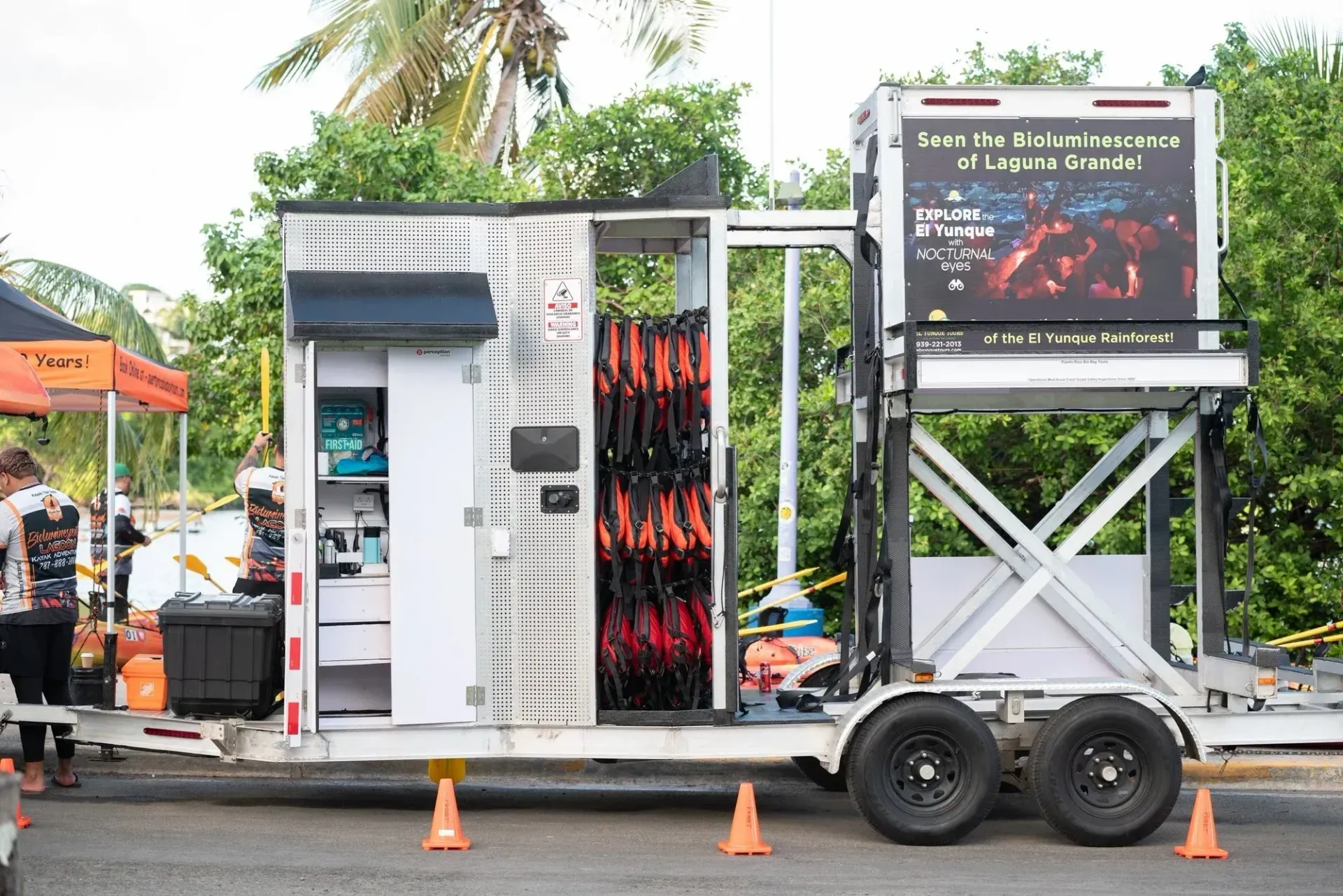 Portable outdoor power unit with screen, cables, and wheels, parked beside orange cones on a road