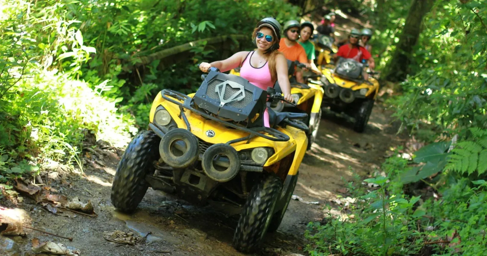 Three people riding yellow ATVs on a muddy forest trail