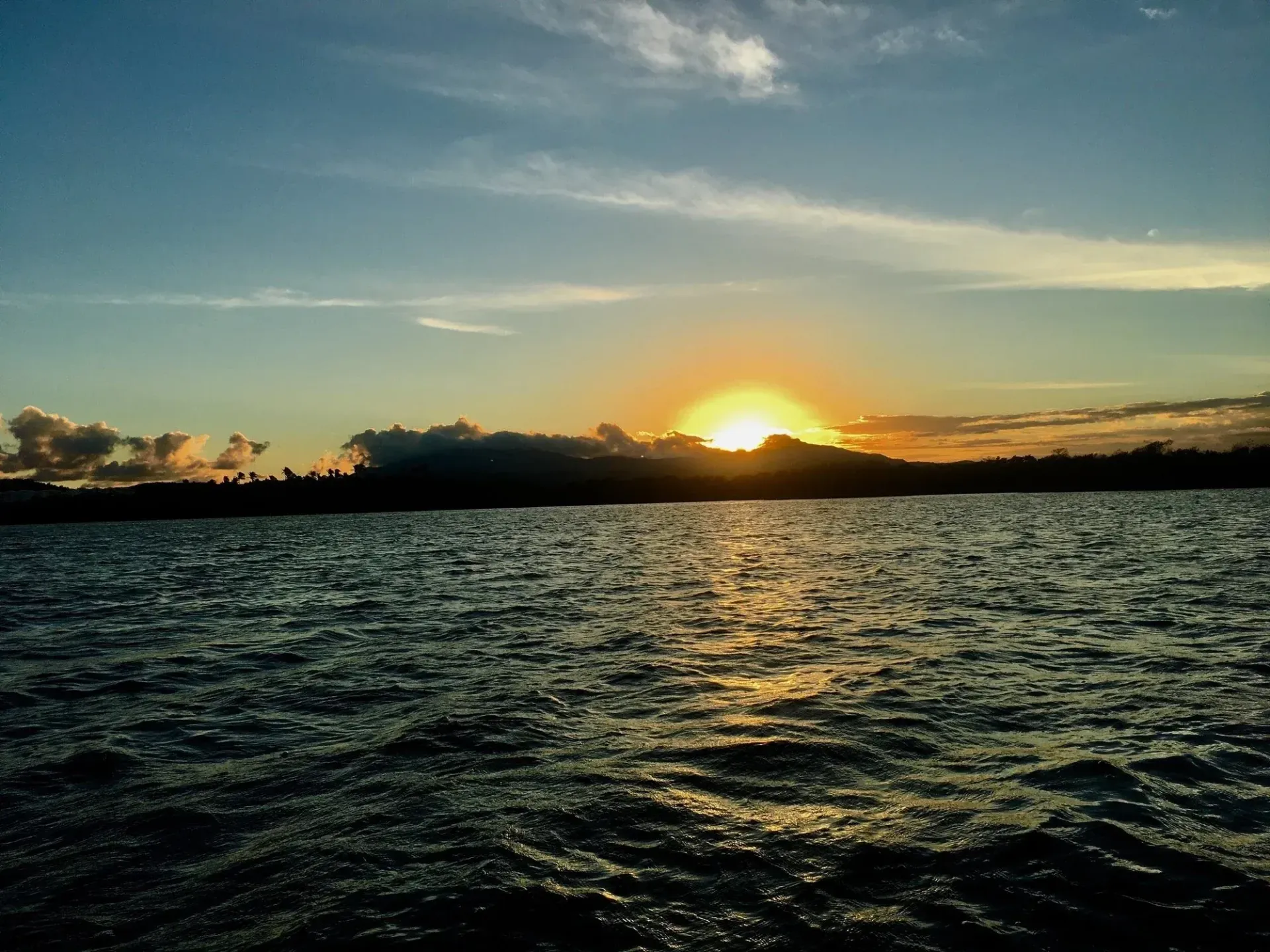 Sunset over rippling water with a glowing horizon and silhouetted shoreline