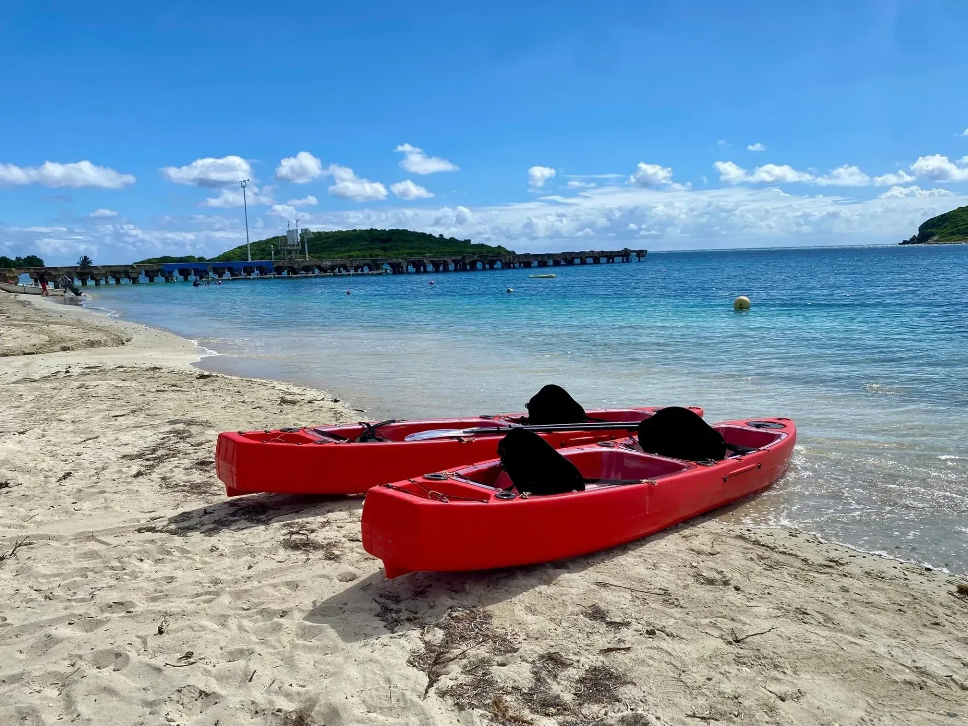 Two red kayaks on a sandy beach beside clear blue water under a sunny sky