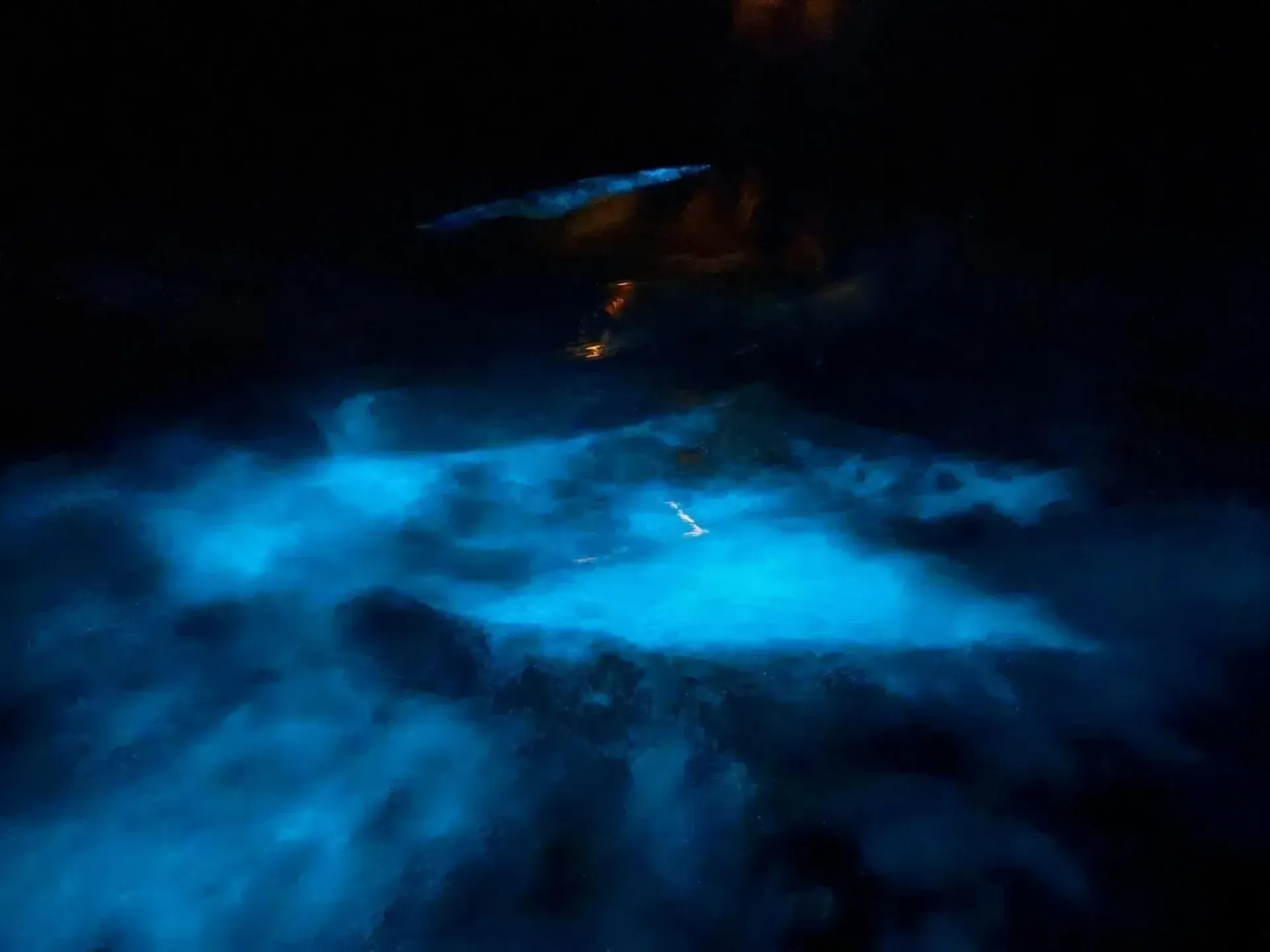 Dark scene with bright blue light reflecting on rippling water or mist.