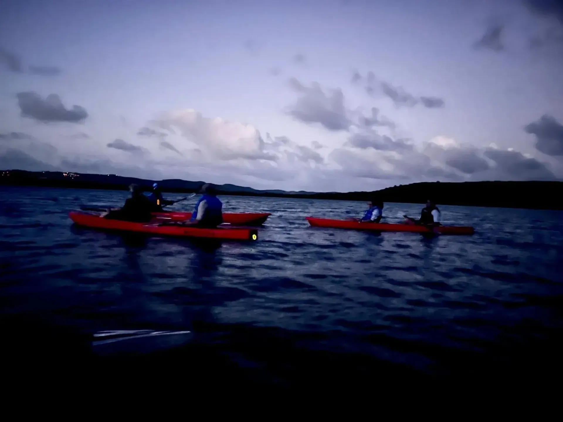 Two red kayaks with paddlers on dark water under a cloudy evening sky