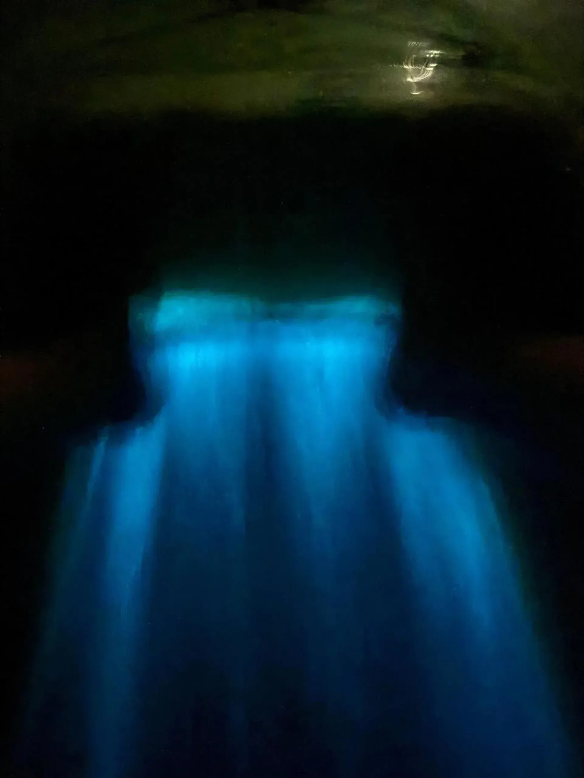 Blue waterfall glowing in a dark cave-like scene