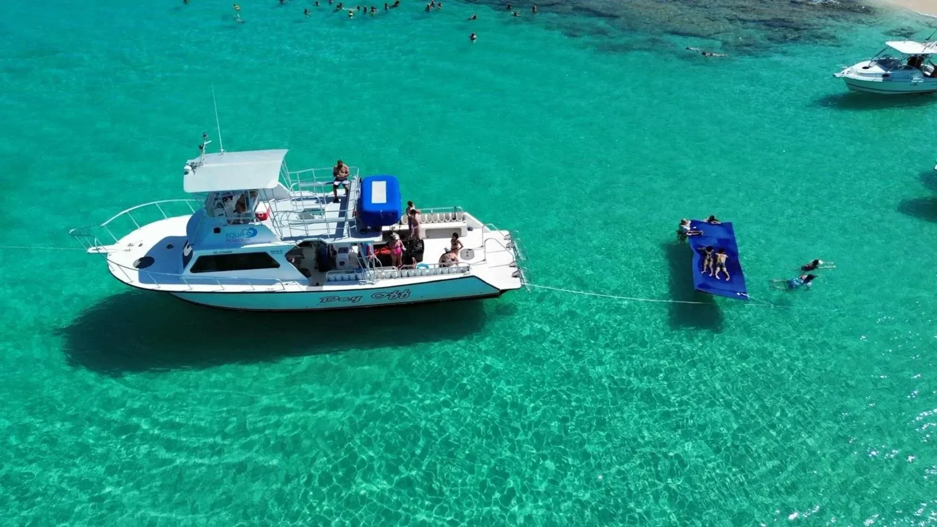 White boat and blue dinghy floating on bright turquoise water, with a swimmer nearby.
