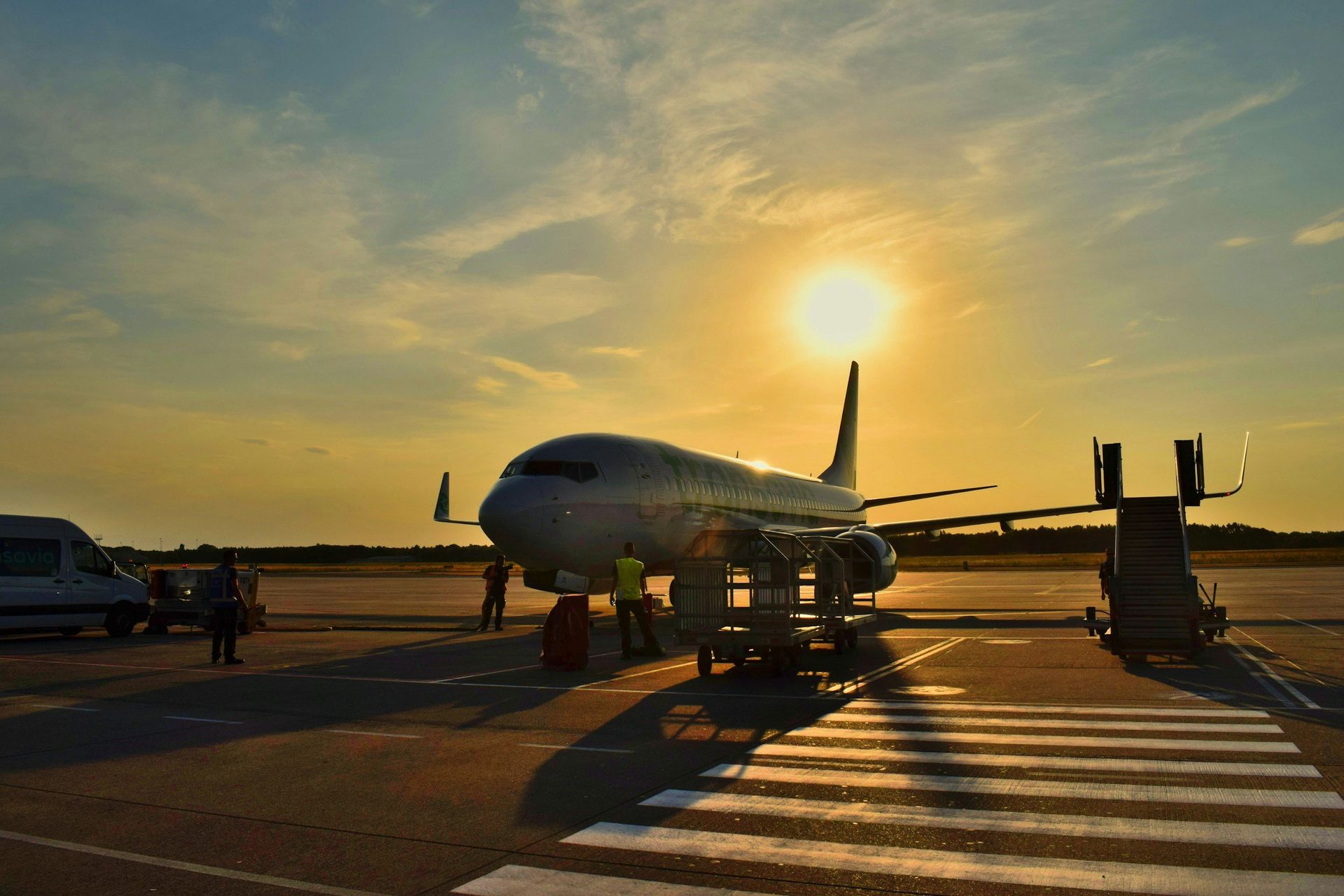 Airplane at sunset on airport tarmac with people and ground equipment near the runway
