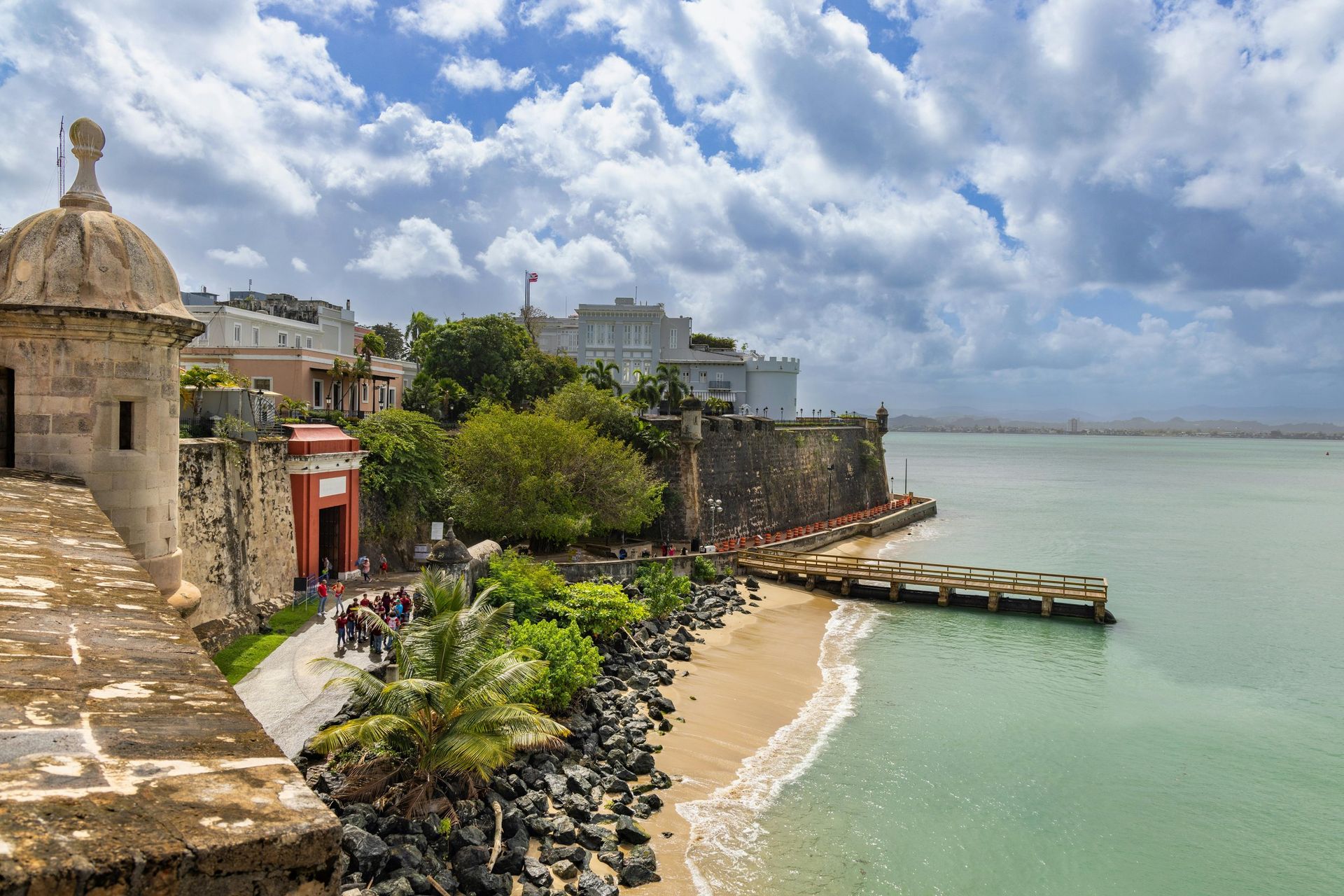 Historic seaside fort overlooking a sandy cove, turquoise water, and a cloudy sky