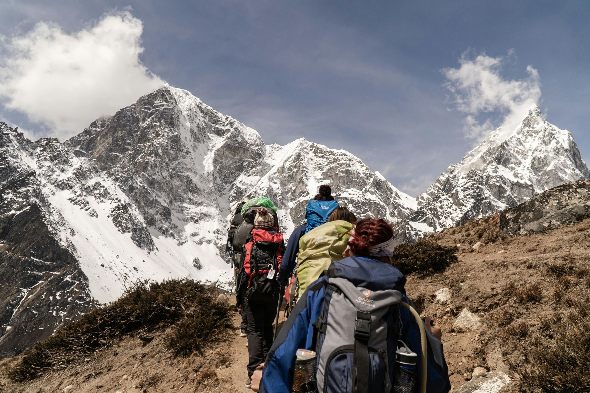 Hikers with backpacks trekking through a snowy mountain pass under a cloudy sky.