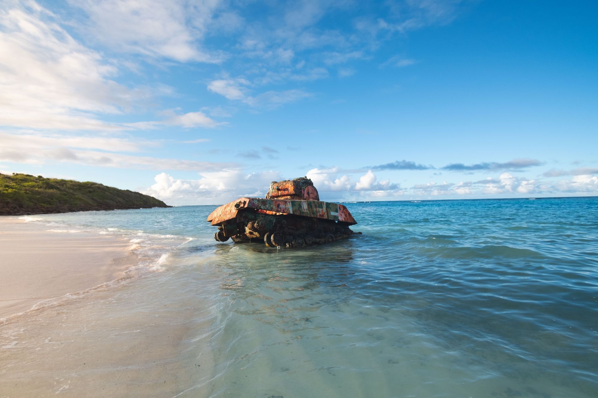 Rocky outcrop in calm blue ocean with sandy beach and distant green headland under a bright sky