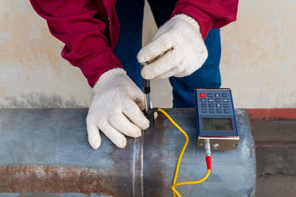 A man is measuring the thickness of a metal pipe — LJ's Technical Services In Burdell, QLD
