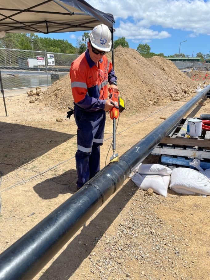A Man In A Hard Hat Is Working On A Pipe — LJ's Technical Services In Burdell, QLD