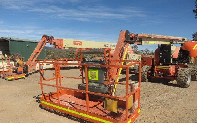 Two Orange Aerial Lifts Are Parked Next To Each Other In A Dirt Field — LJ's Technical Services In Burdell, QLD
