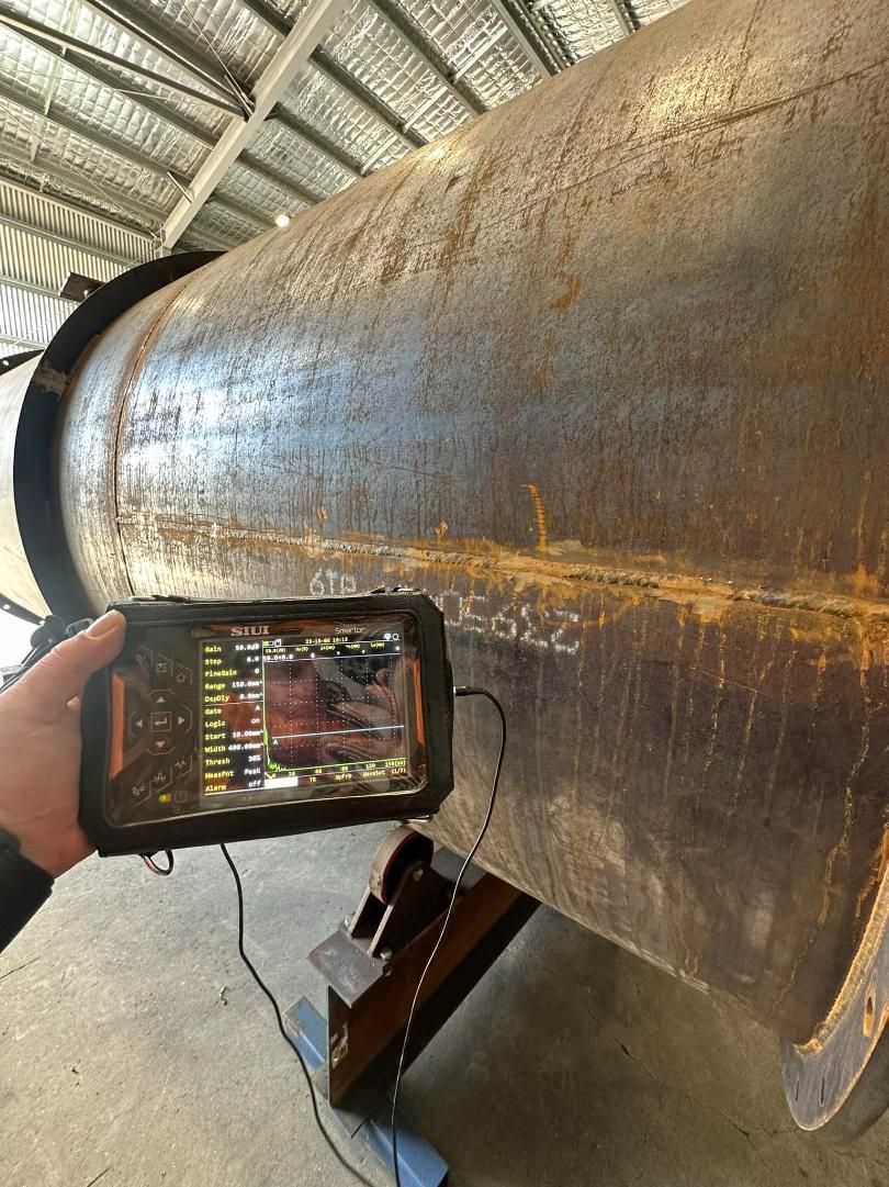 A Person Is Holding A Cell Phone In Front Of A Large Metal Pipe — LJ's Technical Services In Burdell, QLD