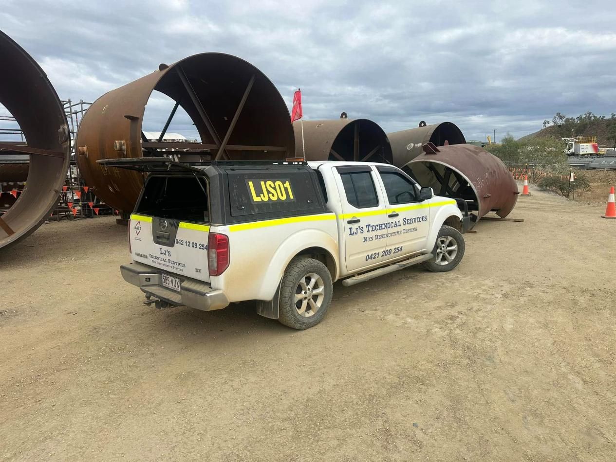 A White Truck Is Parked In A Dirt Field Next To Large Pipes — LJ's Technical Services In Burdell, QLD
