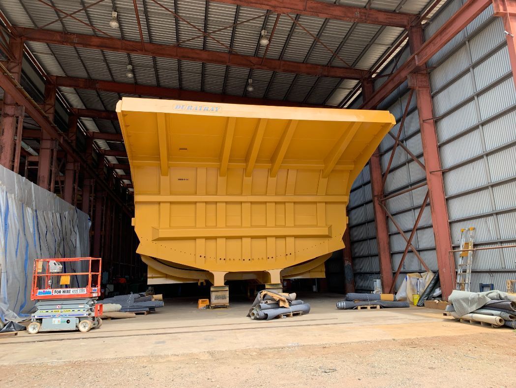 A Large Yellow Dump Truck is Sitting Inside of a Large Building — LJ's Technical Services In Burdell, QLD