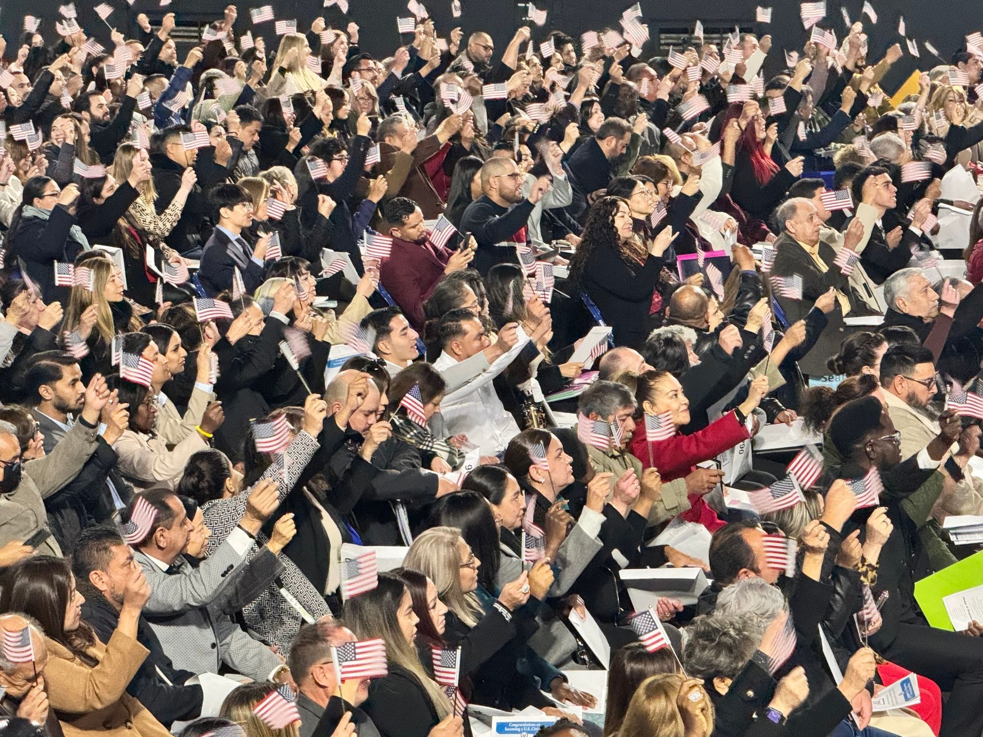Large crowd cheering, many waving small American flags.