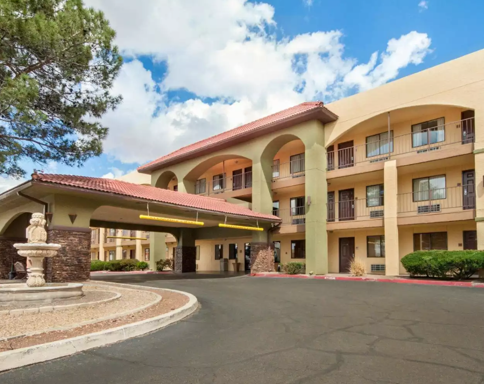 Hotel exterior with arched entrance, fountain, and multi-story building. Beige and brown color scheme with a blue sky.