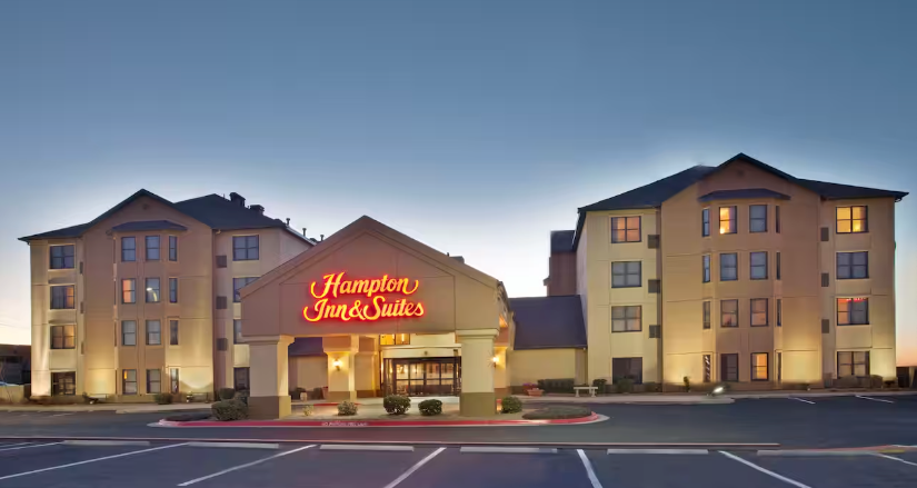 Hampton Inn & Suites hotel entrance at dusk with lighted signage, tan exterior, and a circular driveway.