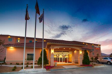 Hotel entrance with flags, tan building, and sky with sunset colors.