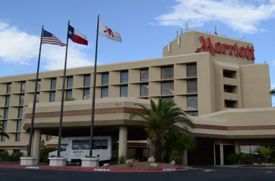 Marriott hotel exterior with flags and a shuttle under a covered entrance in front of the building.