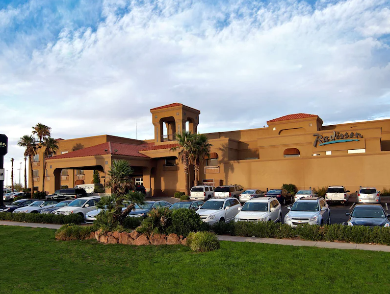 Casino building with a large parking lot and a grassy area. The sky is partly cloudy.