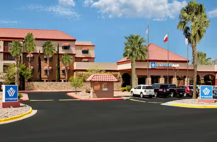 Hotel exterior with palm trees, a red tile roof, and a parking area.