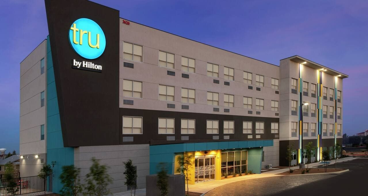 Tru by Hilton hotel exterior at dusk; teal and gray facade, illuminated sign.
