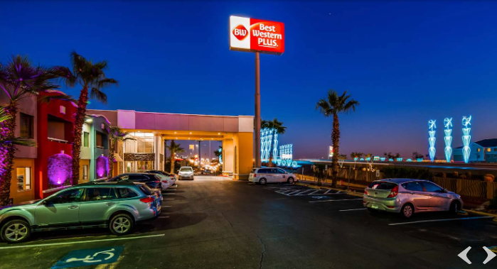 Best Western Plus hotel at night, lit sign above entrance, cars parked in front.