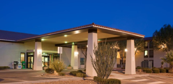 Hotel entrance under a canopy with supporting pillars, dusk lighting.