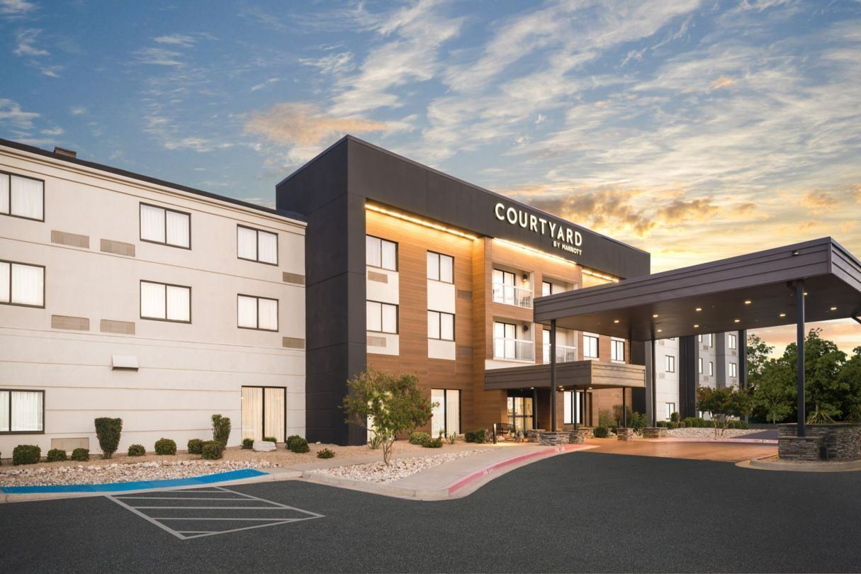 Courtyard hotel exterior with parking, signage, and a covered entrance against a sunset sky.