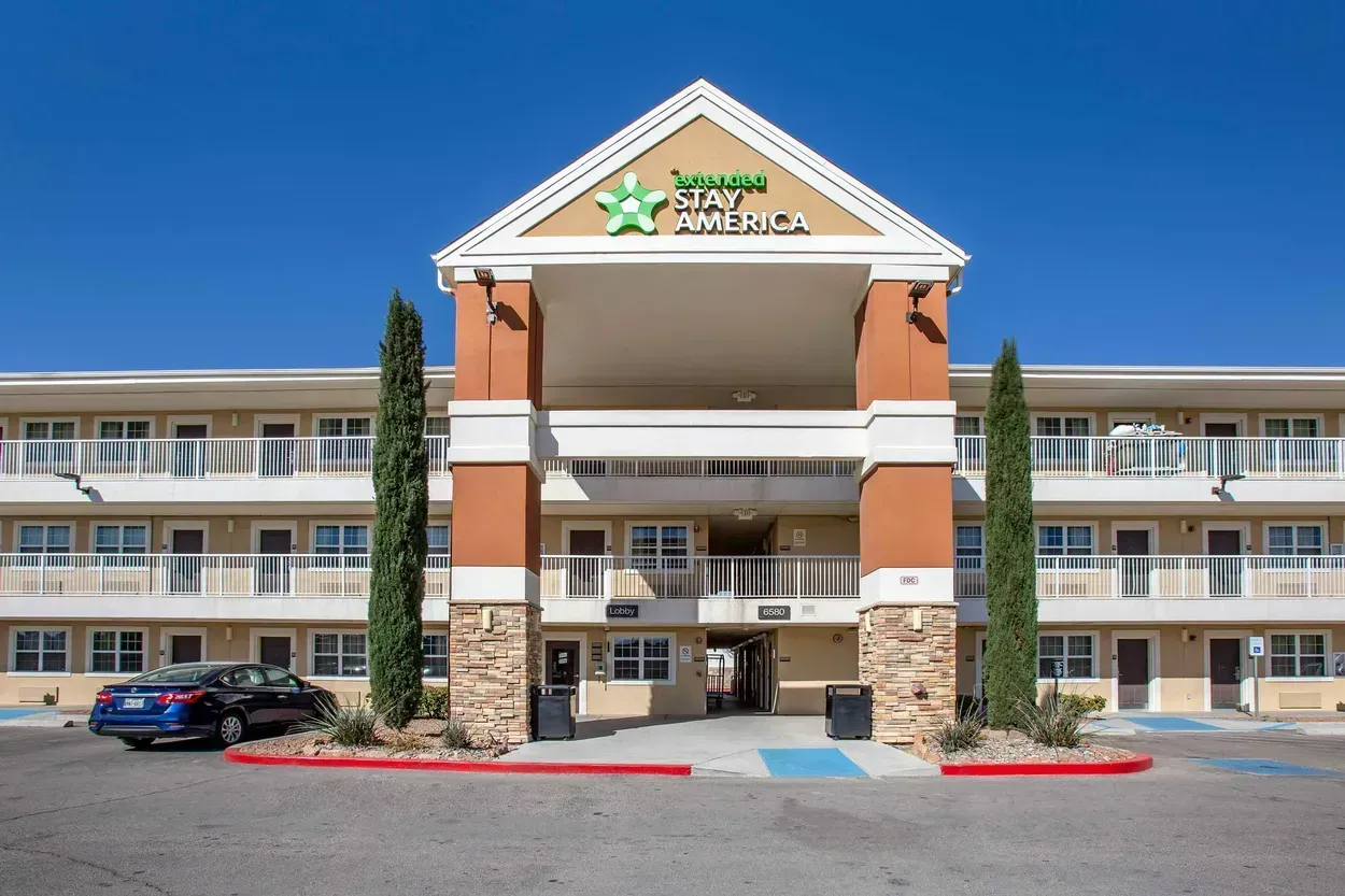 Exterior of an Extended Stay America hotel with a blue sky; a car is parked in front.